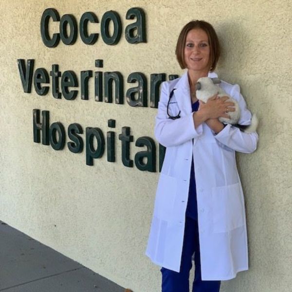 Dr. Brennan standing by Cocoa Veterinary Hospital sign holding small animal